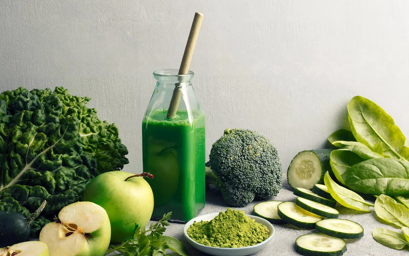Grønn smoothie, grønne grønnsaker og frukt på et bord