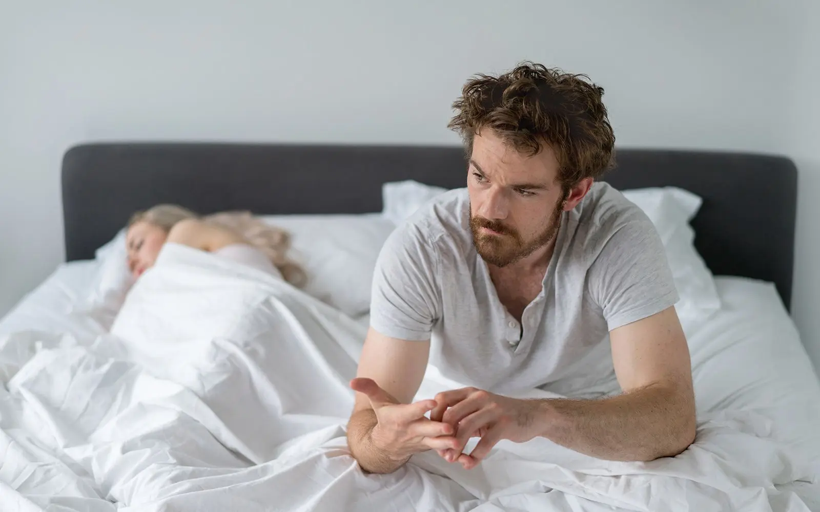 Mann sittende i sengen med en kvinne sovende ved siden av