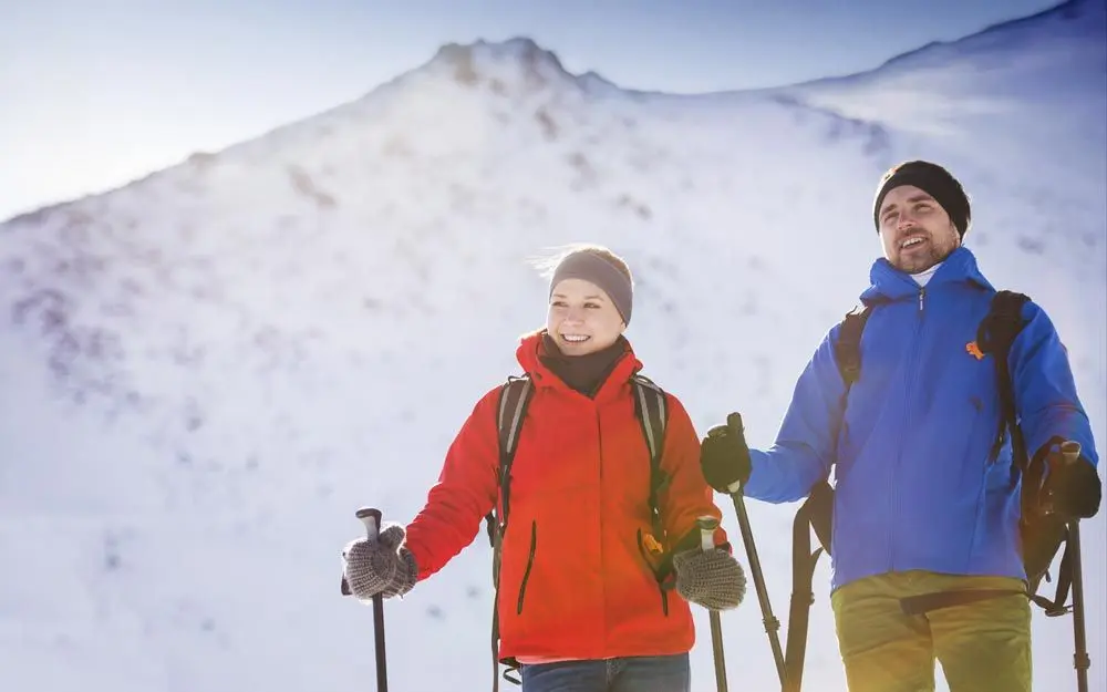 Bilde av en kvinne og en mann som med ski og ryggsekk stående med snødekt fjell i bakgrunnen.