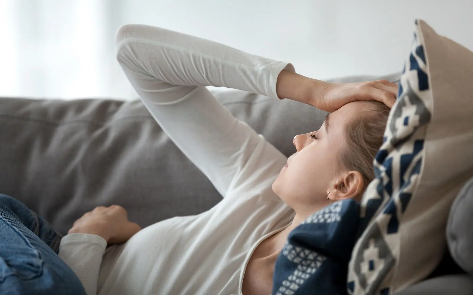 Kvinne med hodepine ligger på en sofa