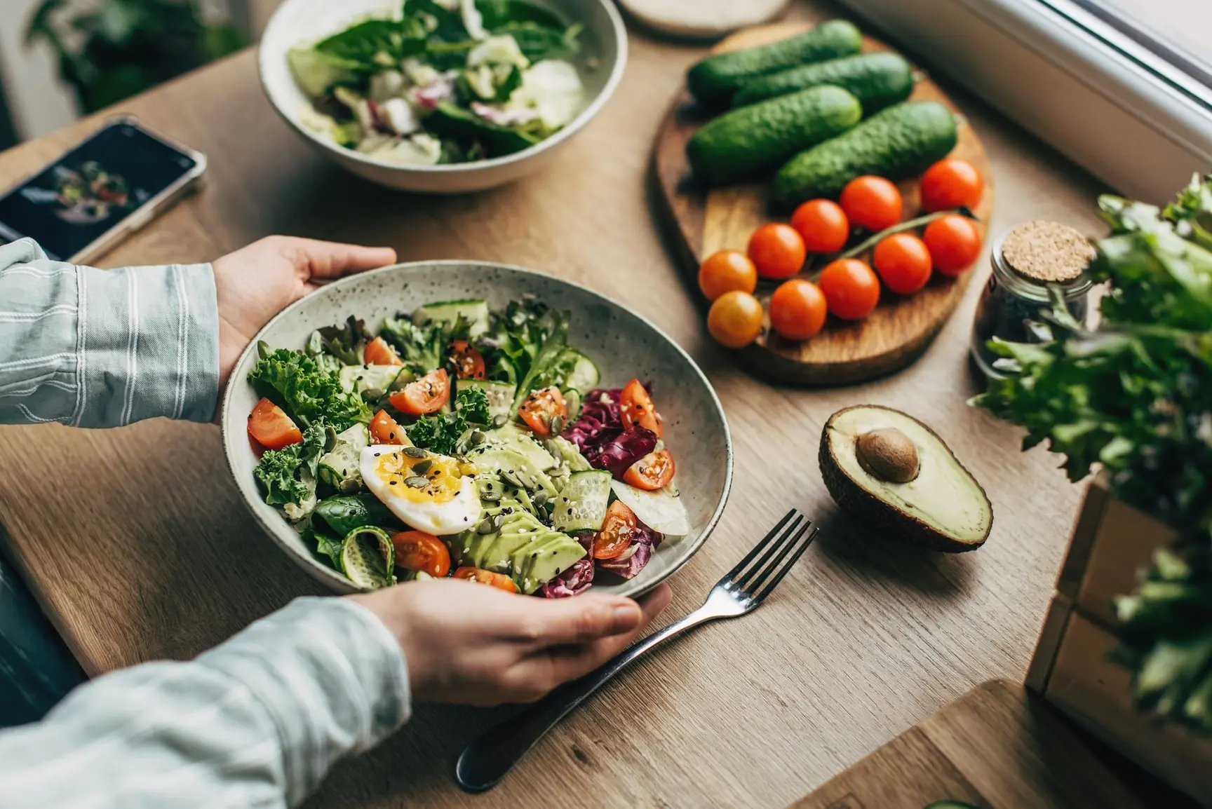 En frisk salat med egg, avokado, tomater, agurk og grønne blader på et bord sammen med ferske grønnsaker.