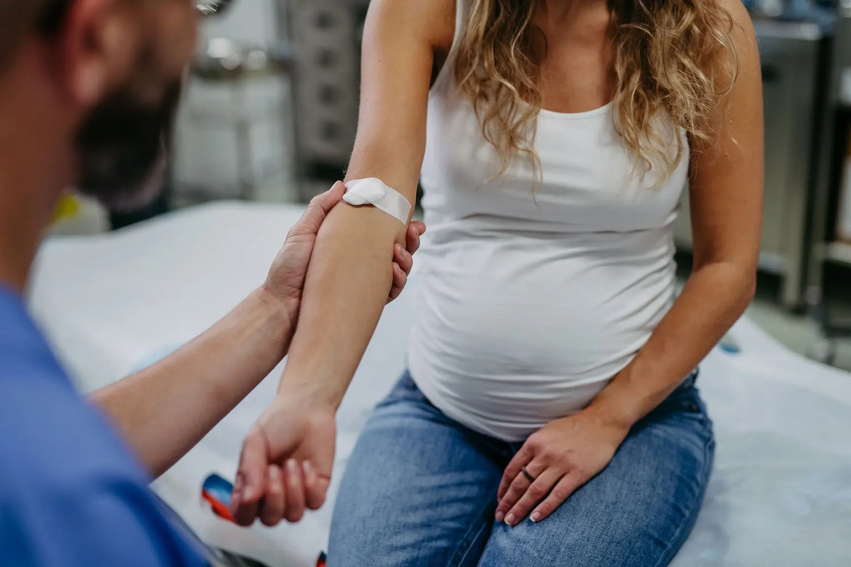En gravid kvinne sitter og holder armen ut med et plaster. En mann i forgrunnen holder henne i armen