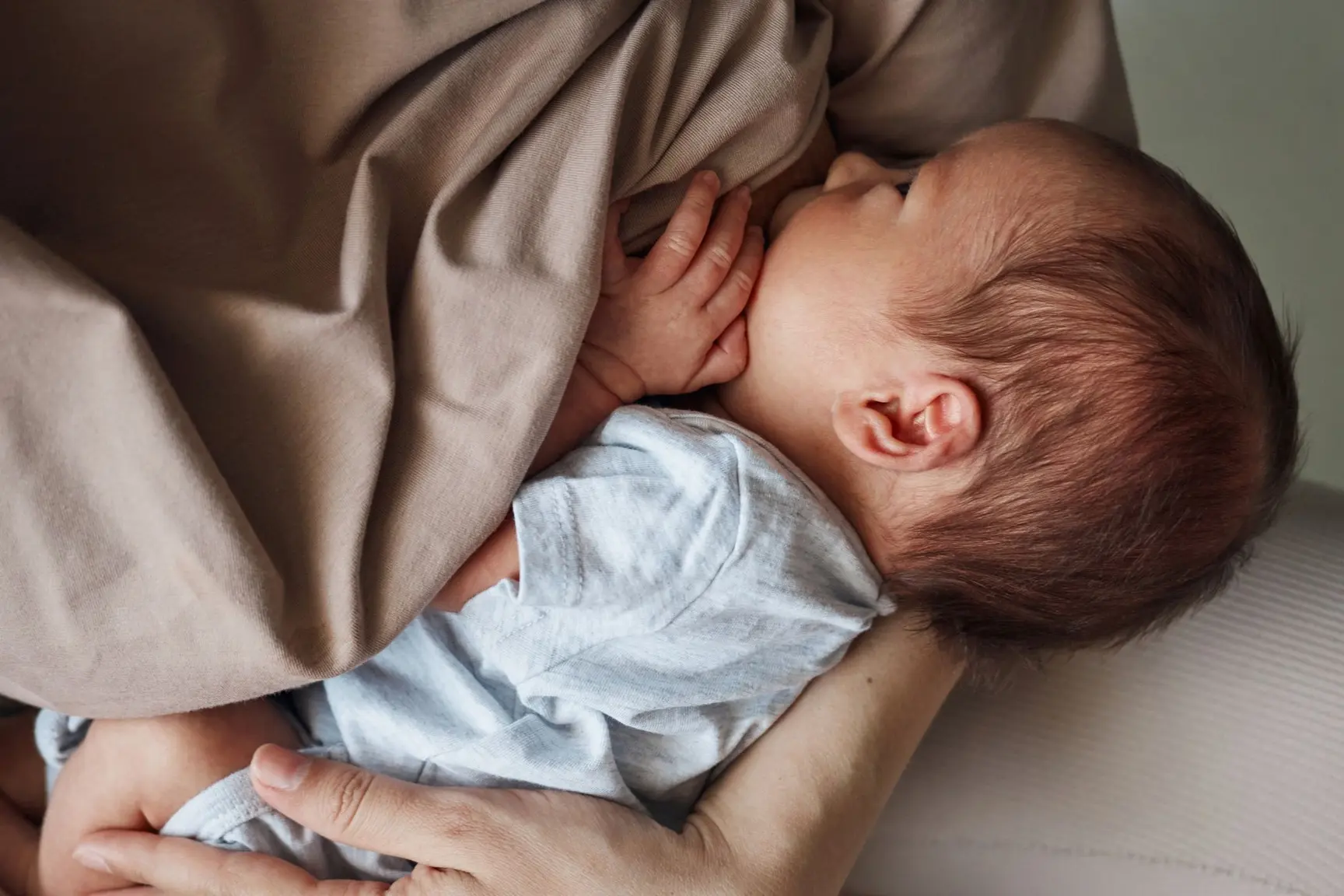 En baby ligger ved brystet og ammer.