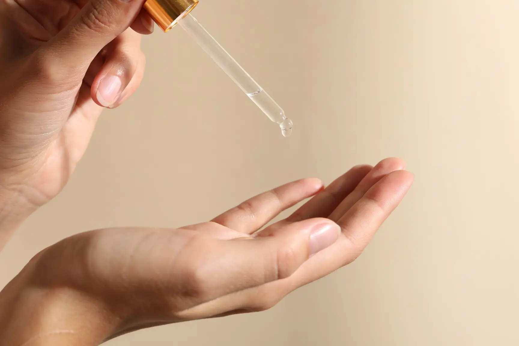 En hånd som holder en pipette med klar hudpleieserum, mens en dråpe slippes ned i den andre hånden.