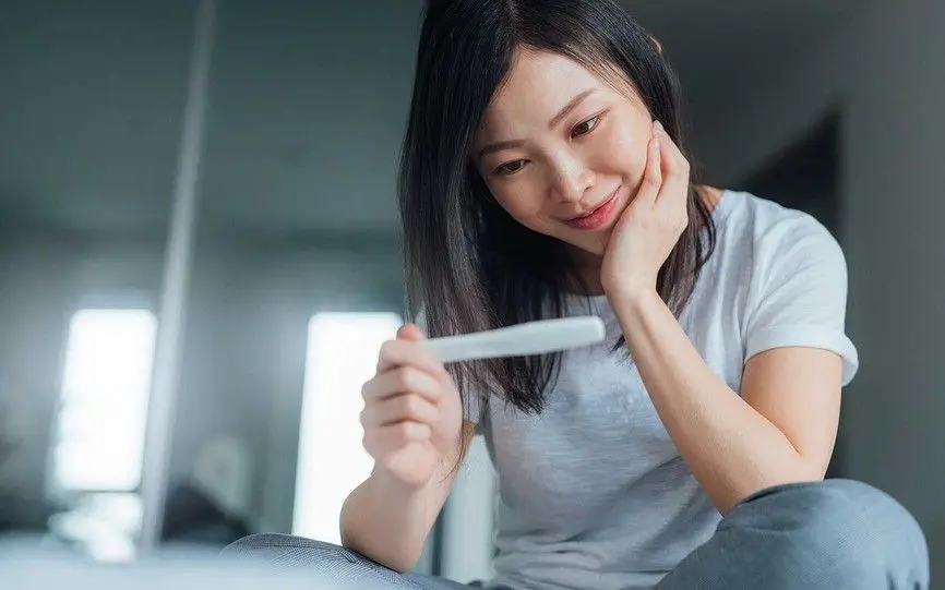 En kvinne smiler mens hun ser på en graviditetstest
