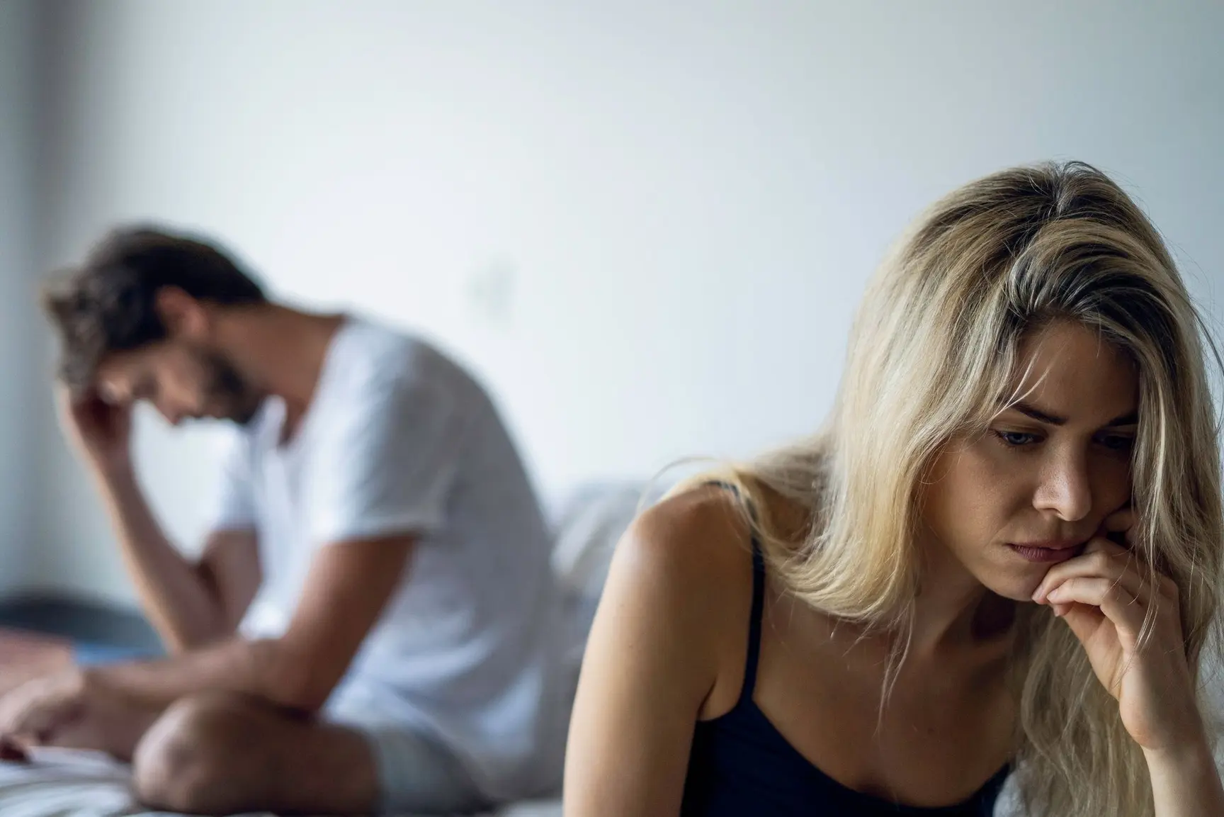 Ungt par sitter på en seng og ser oppgitt ut