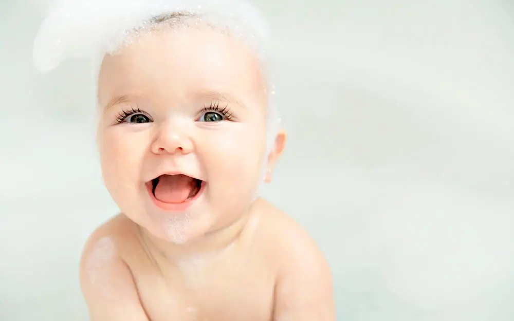 Nærbilde av en smilende baby i badekaret med såpeskum på hodet