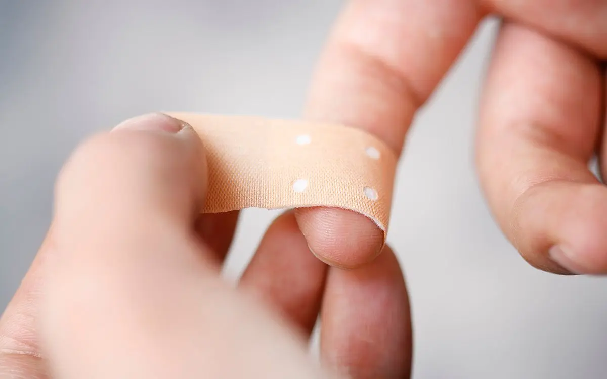 En person som påfører et lysebrunt fingerplaster rundt tuppen av den ene pekefingeren sin.