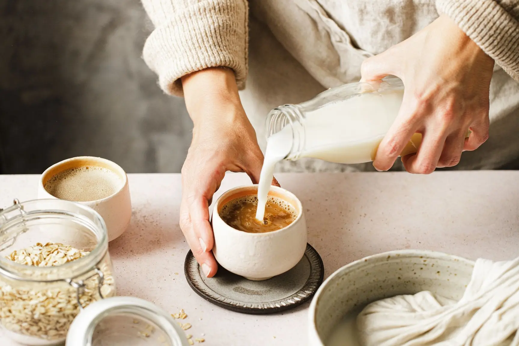 En kvinne holder en kopp med kaffe og heller i melk