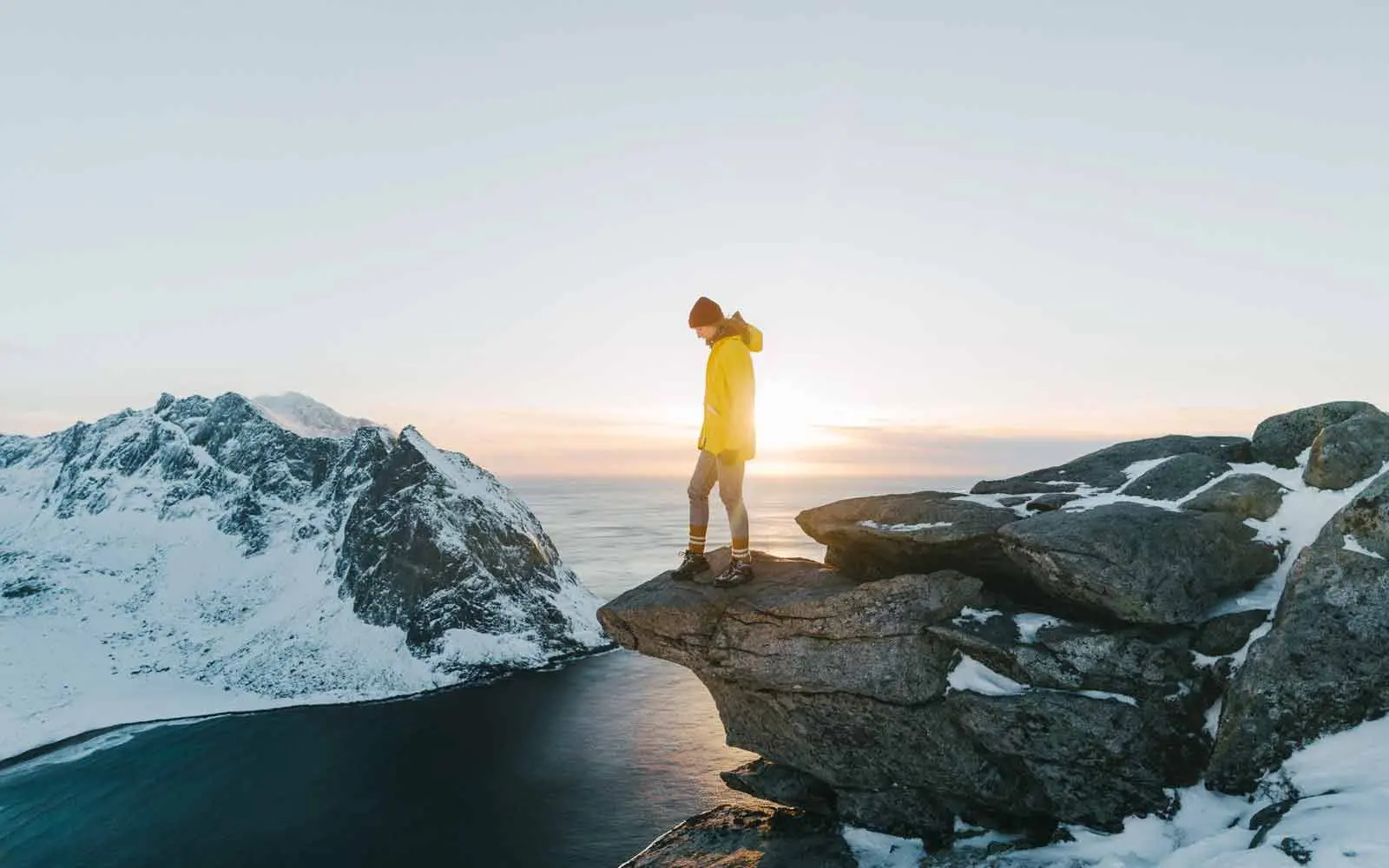En kvinne står på en klippe og ser utover snødekte fjell og sjø