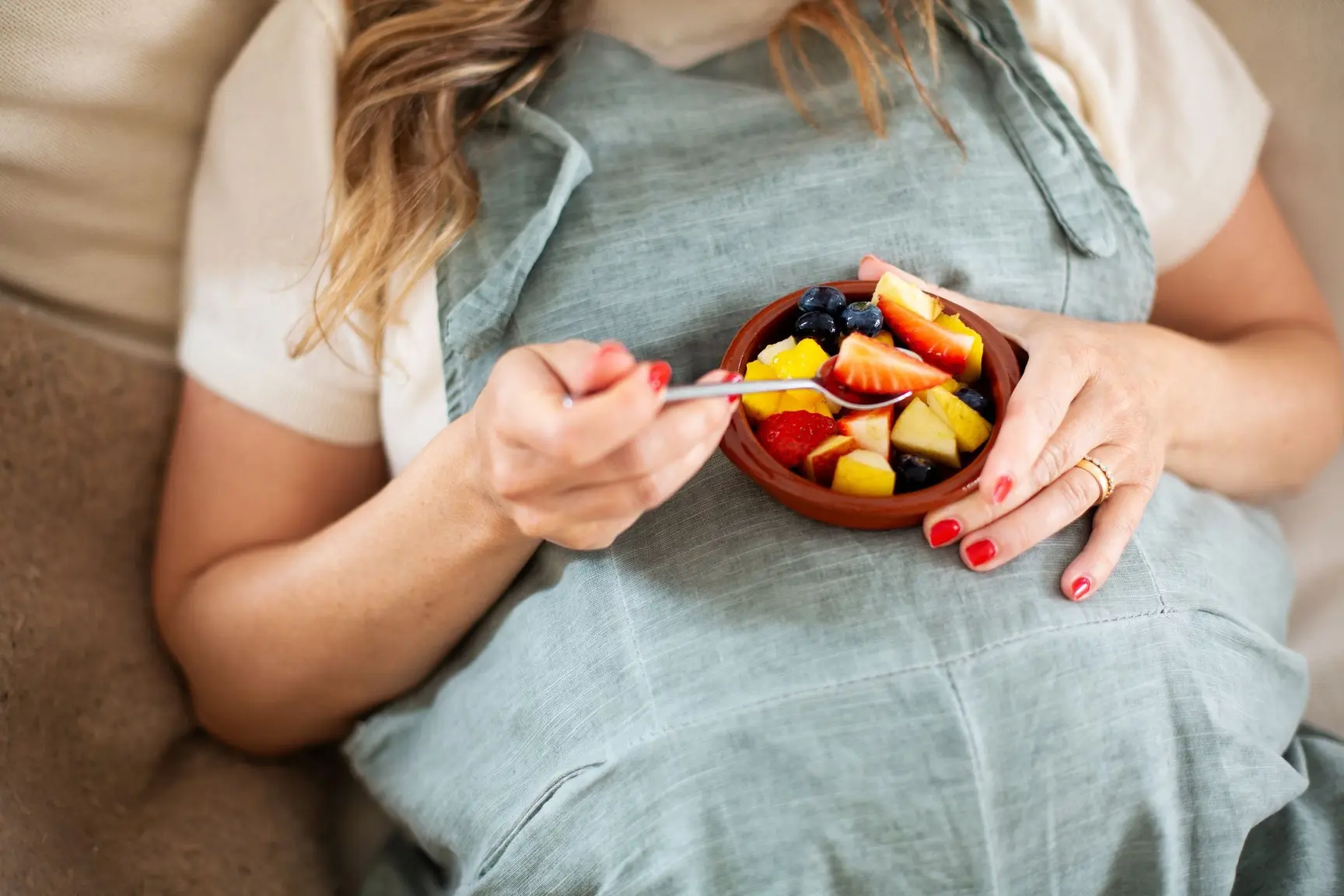 En gravid kvinne spiser en bolle med frisk frukt.
