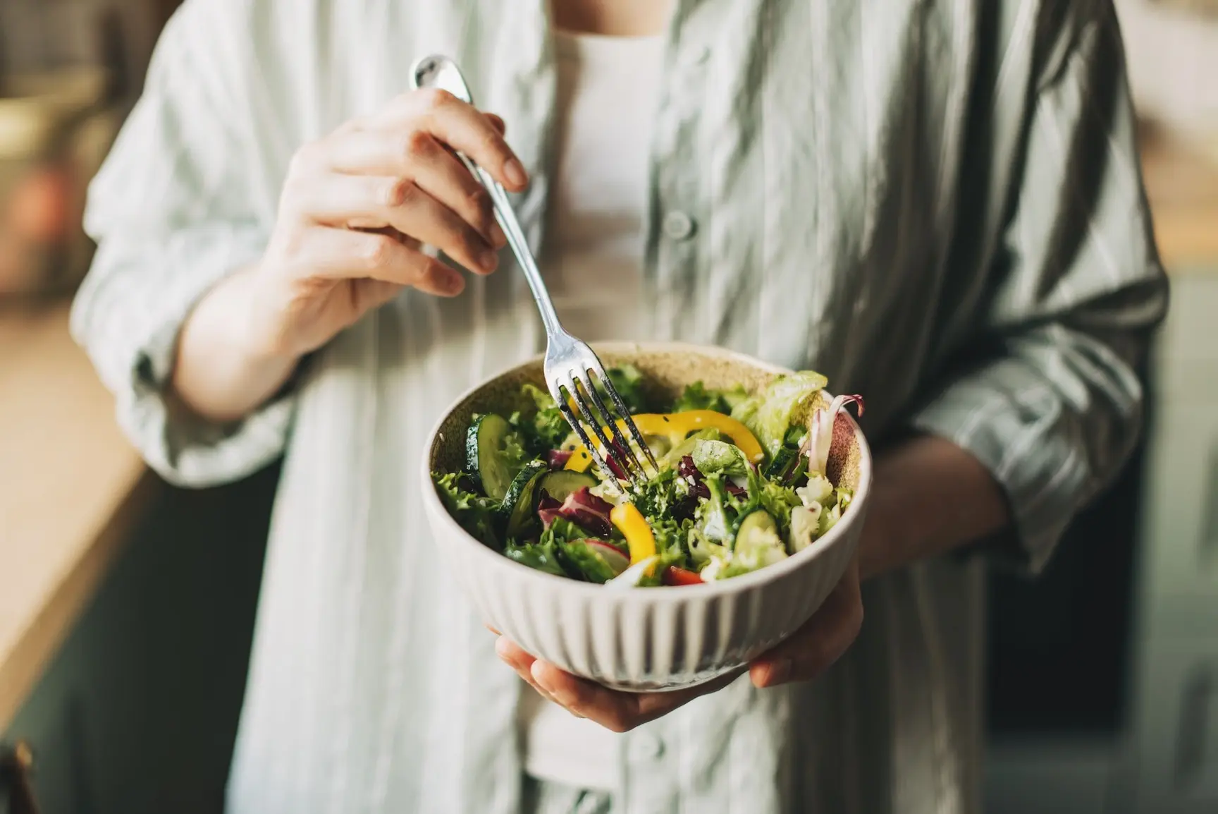 En person holder en bolle med salat i en hånd og en gaffel i den andre