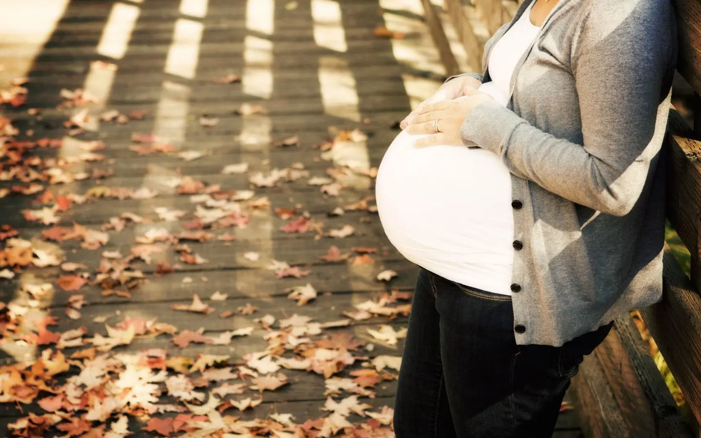 En gravid person som lener seg mot et gjerde og holder begge hendene på magen.