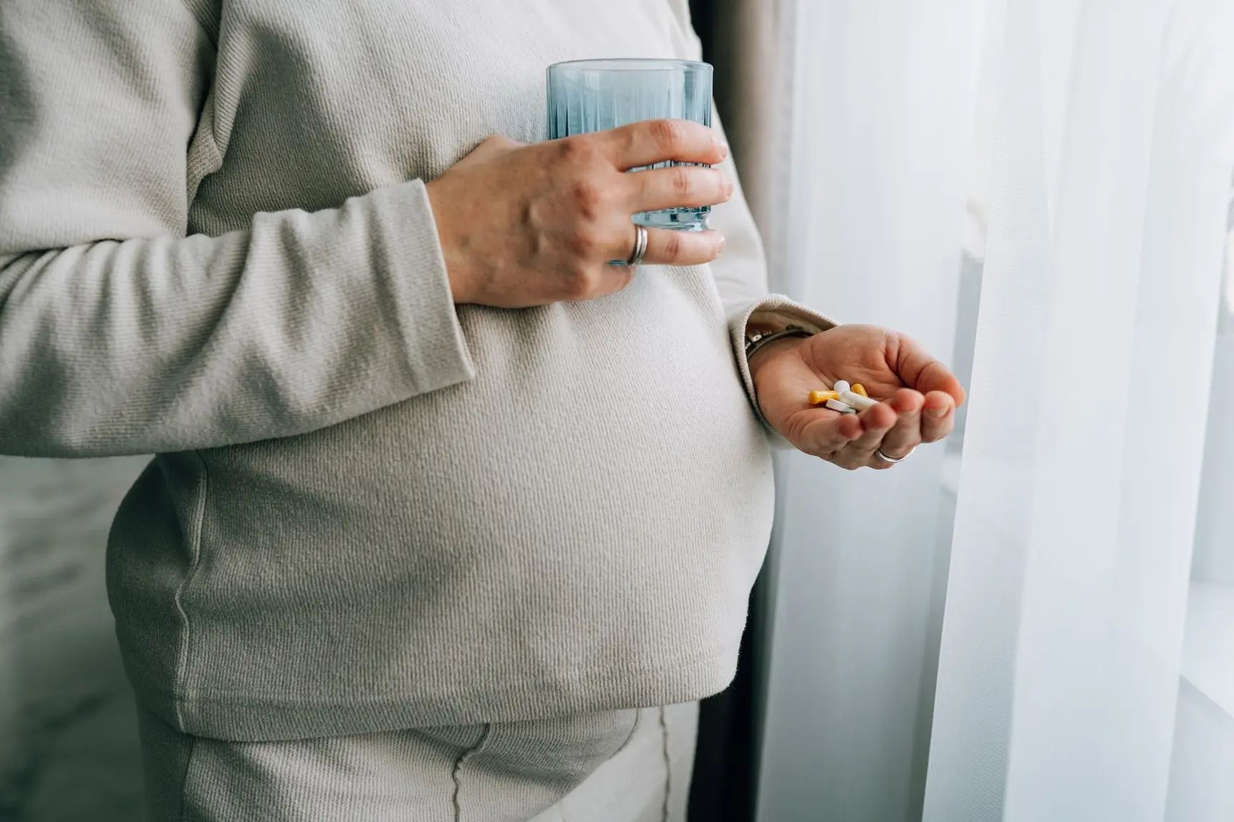 En gravid kvinne står med piller i en hånd og et glass vann i den andre