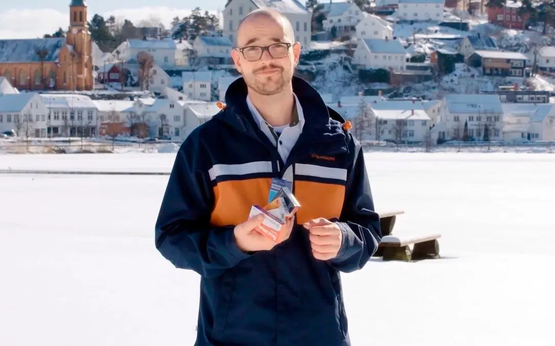 En mann som står ute på vinteren og holder på esker med smertestillende tabletter.