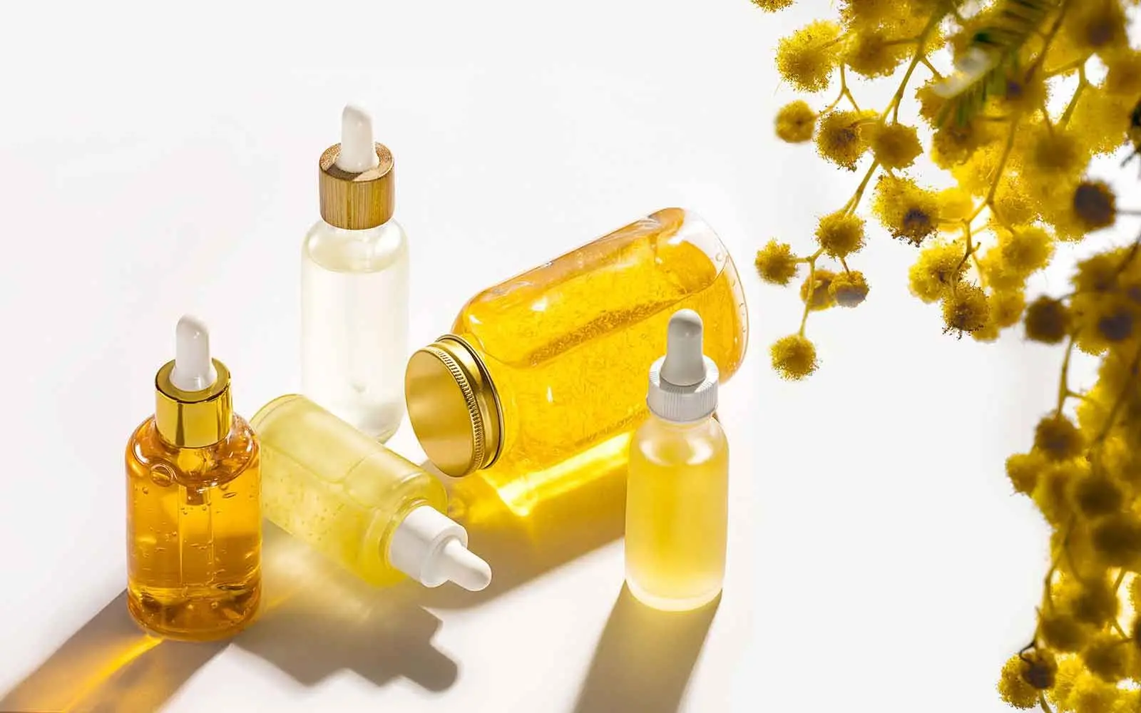 4 pipetteflasker med hudpleieoljer i ulike gule nyanser på hvit bakgrunn. Vitamin E er fettløselig og godt egnet til hudpleieformuleringer som olje og krem.
