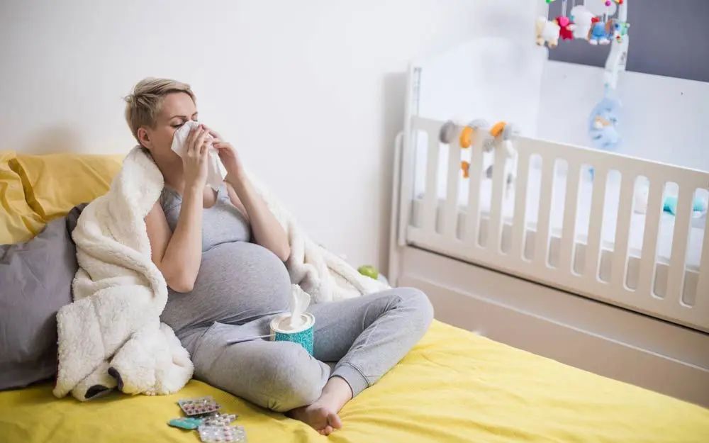 Gravid person som sitter på sengen og holder et lommetørkle på nesen