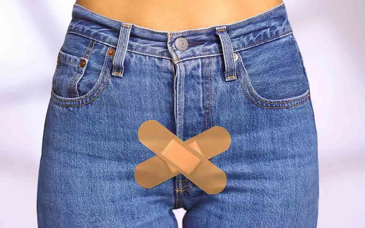 Person iført jeans med to plaster krysset over underlivsområdet – symbol på intim ubehag eller sårhet.