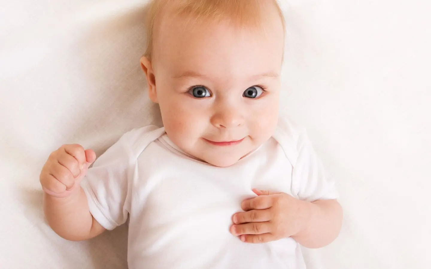 En baby med hvit genser som ser smilende mot kamera