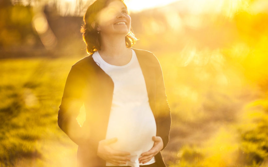 Bilde av en gravid dame som ser mot solen og holder seg rundt magen.