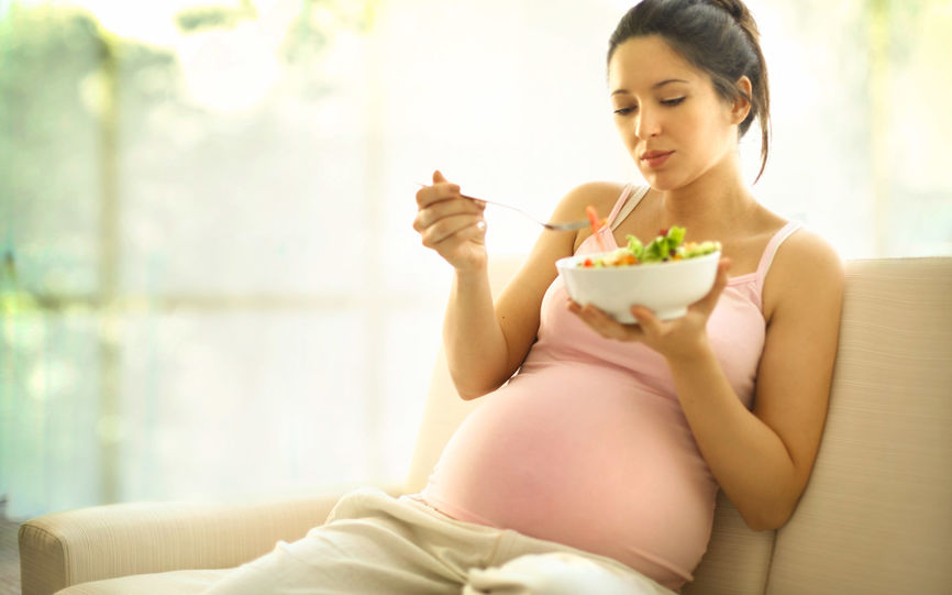 Bilde av en gravid dame som spiser mat fra en skål.