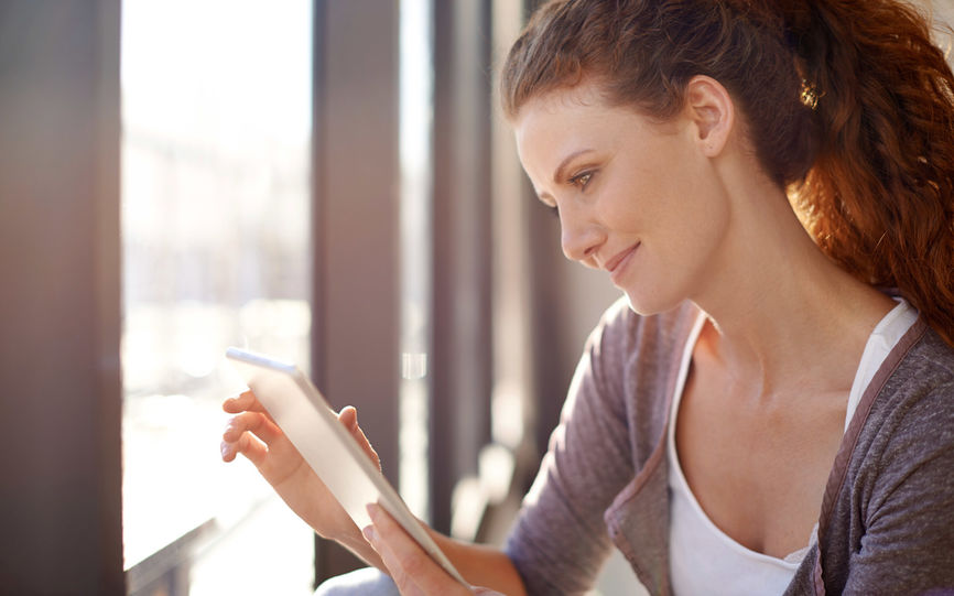 Bilde av en dame som leser på et lesebrett ved et vindu.