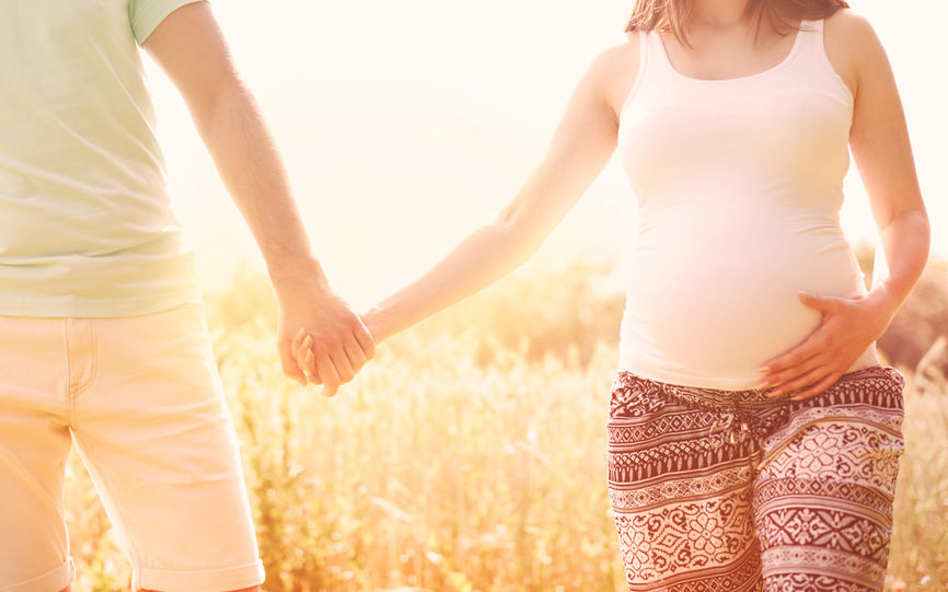En kvinne og en mann holder hender, kvinnen er gravid og holder en hånd på magen.