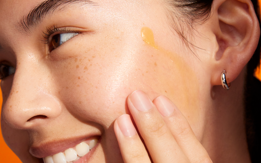 En ung kvinne med fregner over nese og kinn har påført Dermalogica Biolumin Night Restore serum over det ene kinnbeinet og smører dette ut med fingrene.