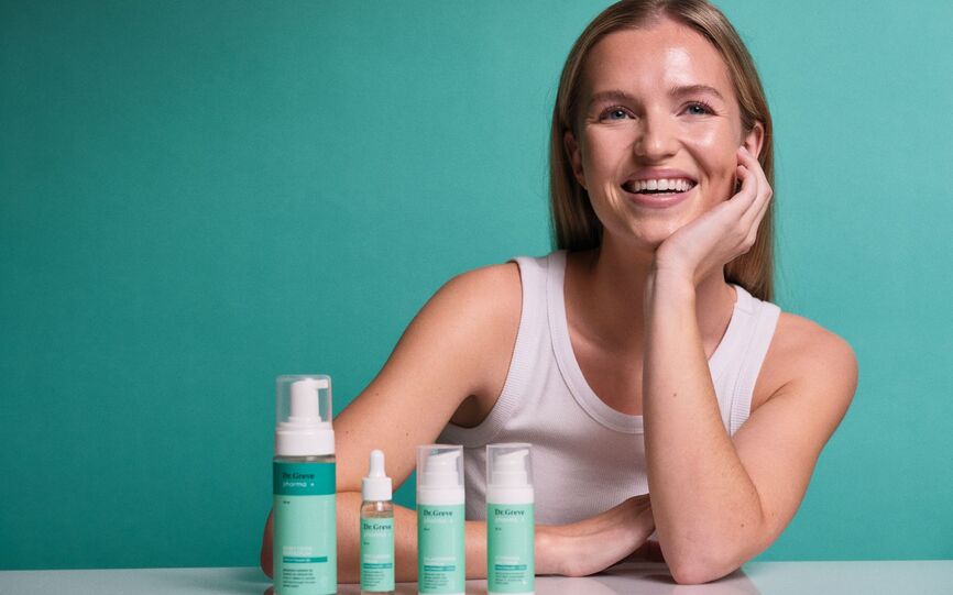 Smilende kvinne hviler hodet i hånden. I forkant står produktserien fra Dr.Greve Pharma