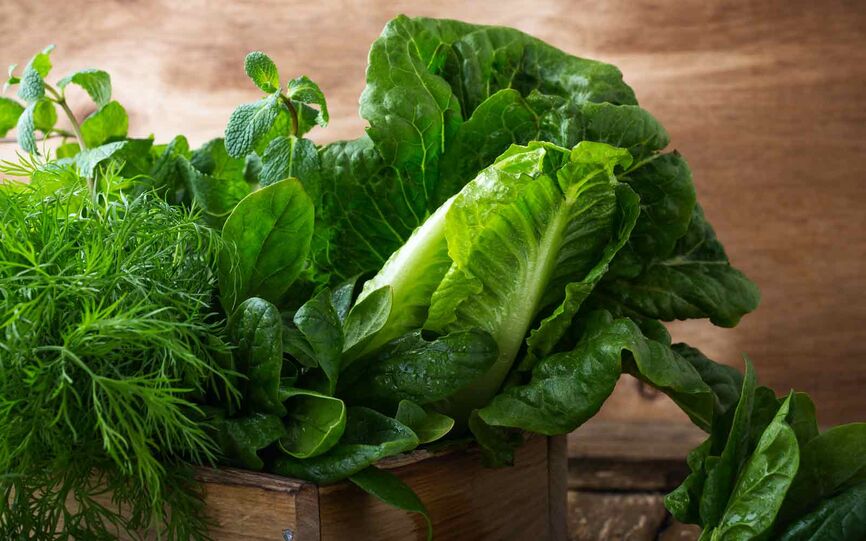 Ulike grønne bladgrønnsaker som hjertesalat, spinat og romanosalat i en rustikk trebolle. Grønne bladgrønnsaker er rike på folat.