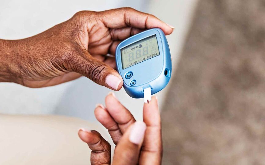 Person som måler blodsukker ved å holde blodsukkeraparat med teststrimmel mot bloddråpe på finger