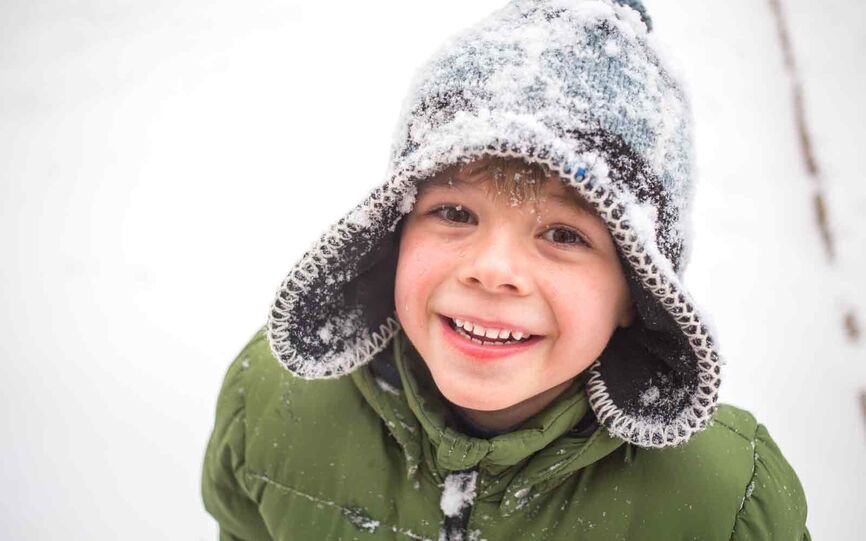 Liten gutt med vinterklær smiler. Luen er dekket med snø