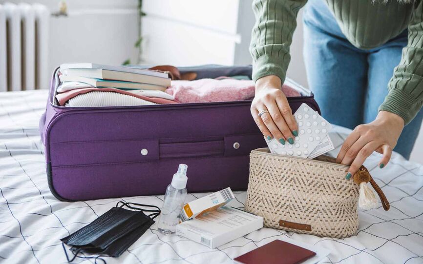 Kvinne pakker med legemidler i toalettmappe. I bakgrunnen ser man en pakket koffert.